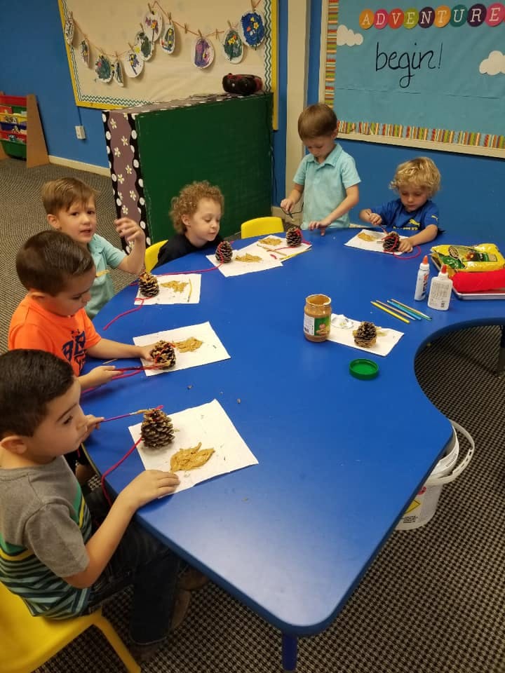 Children sitting at a blue table doing crafts with pinecones and leaves