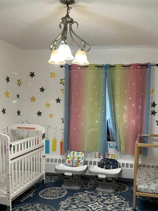 Nursery room with a crib, two high chairs, and rainbow curtains