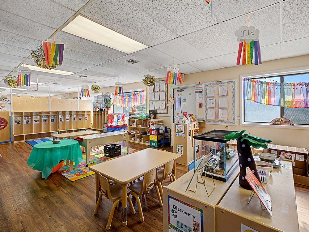 Empty classroom with small tables and chairs, cubbies, and colorful decorations