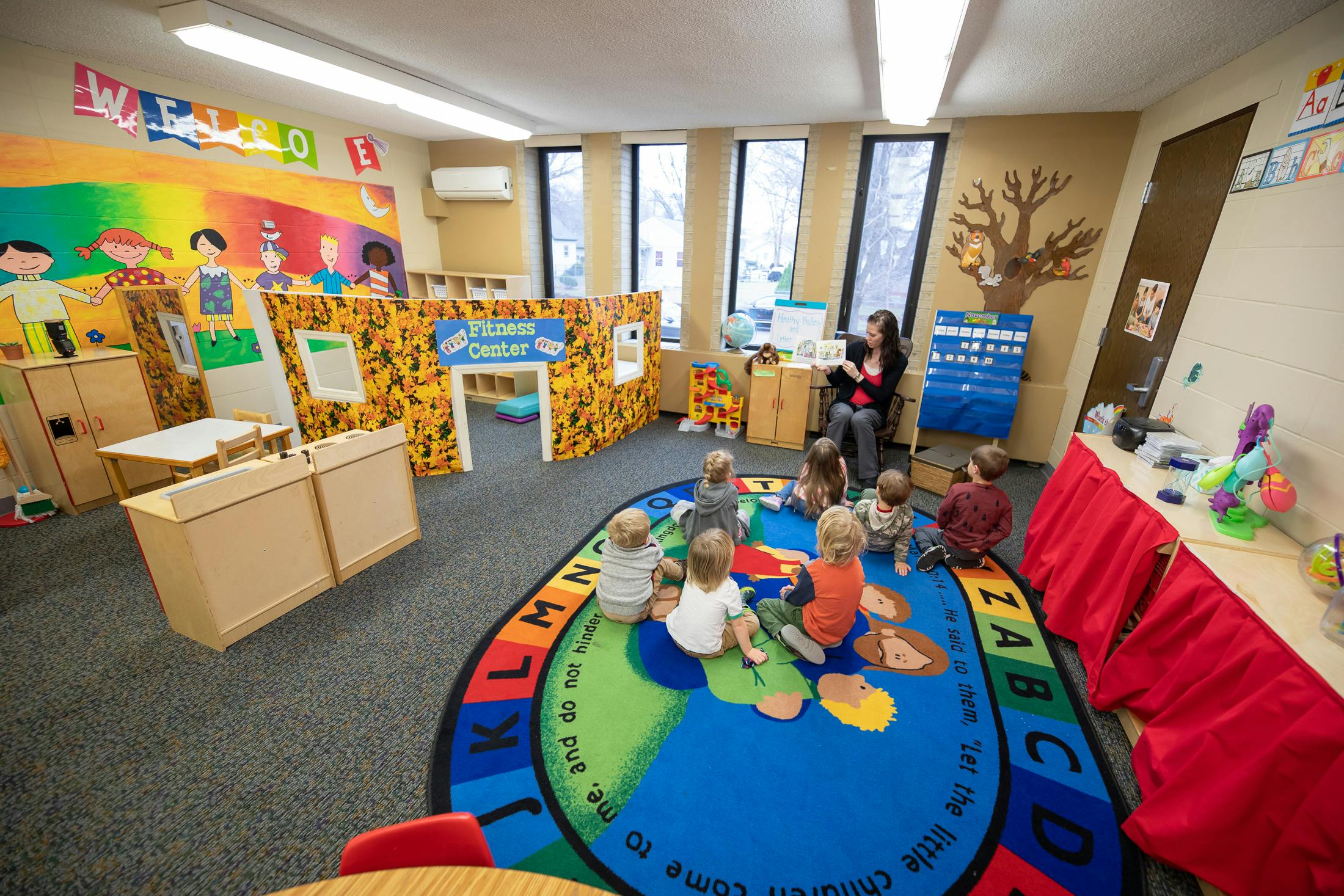 Adult reading to children sitting on a colorful rug in a classroom