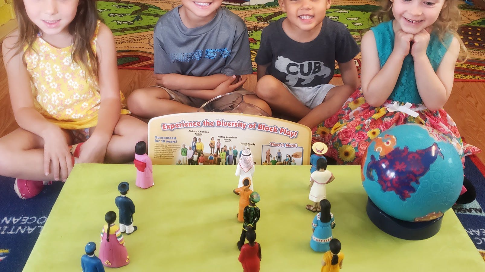 Four children sitting behind a table with figurines and a globe