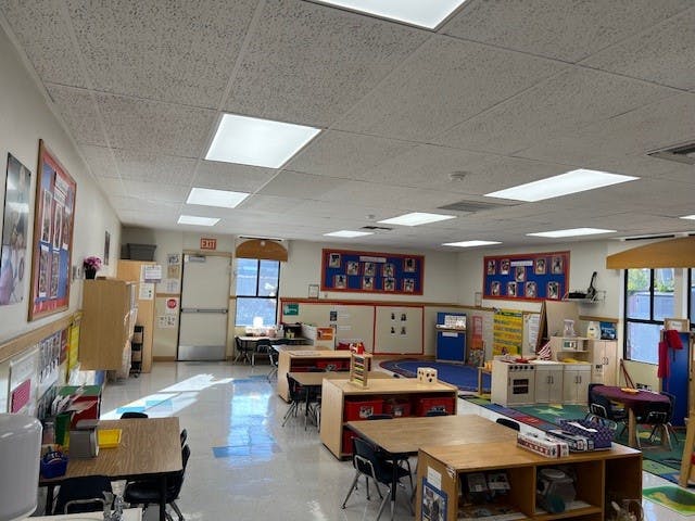 Empty classroom with small tables and chairs, play kitchen, and decorations