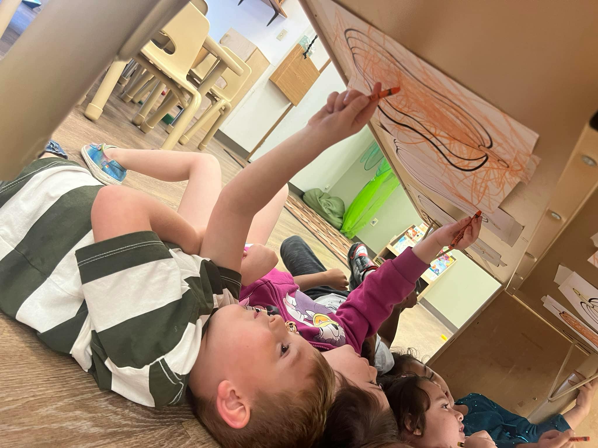 Children lying down and coloring on a large piece of cardboard