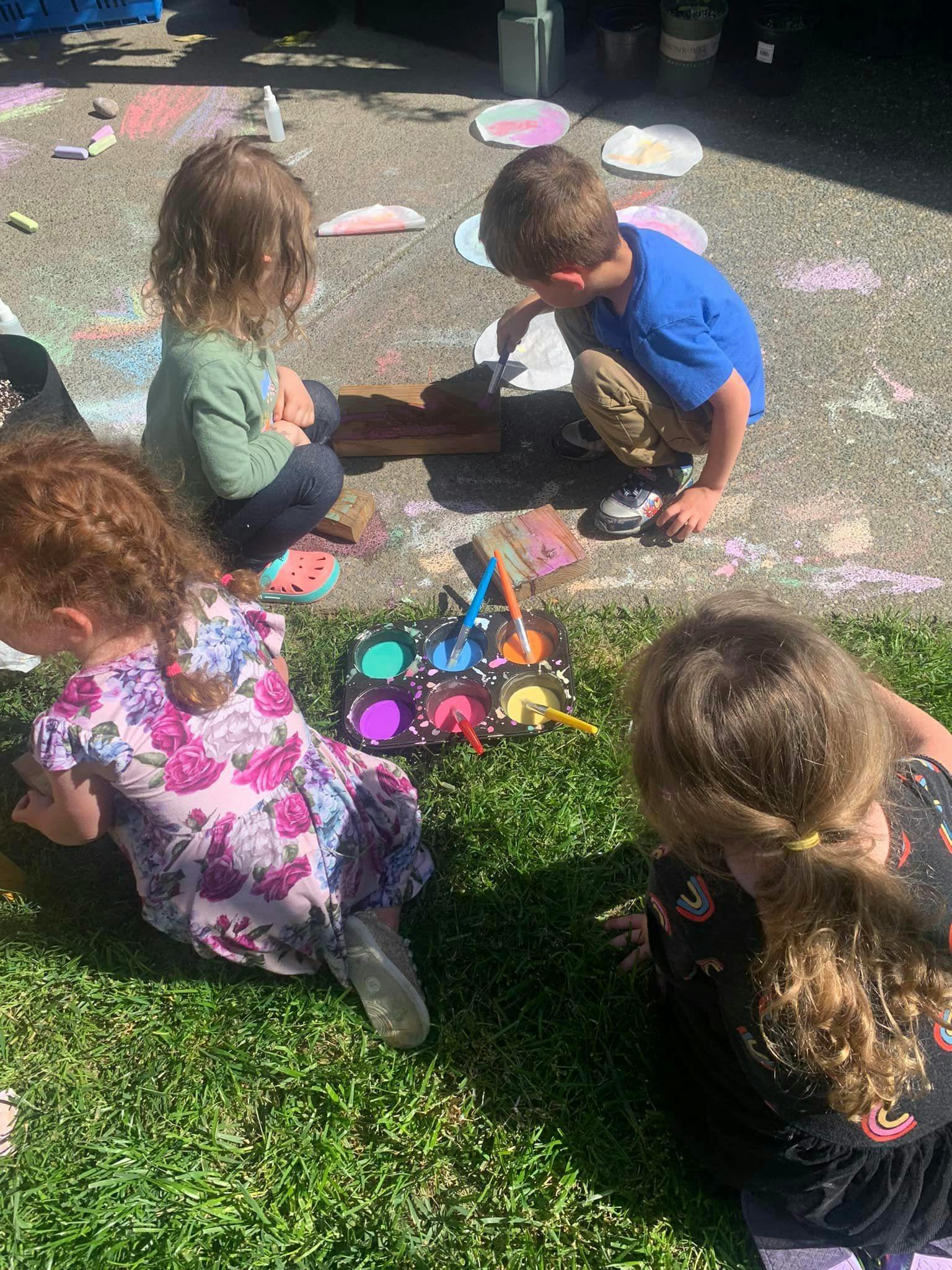 Four children painting outdoors with colorful paints