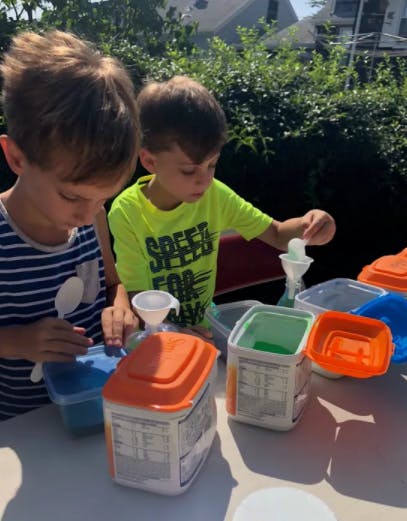 Two children playing with containers and funnels outdoors