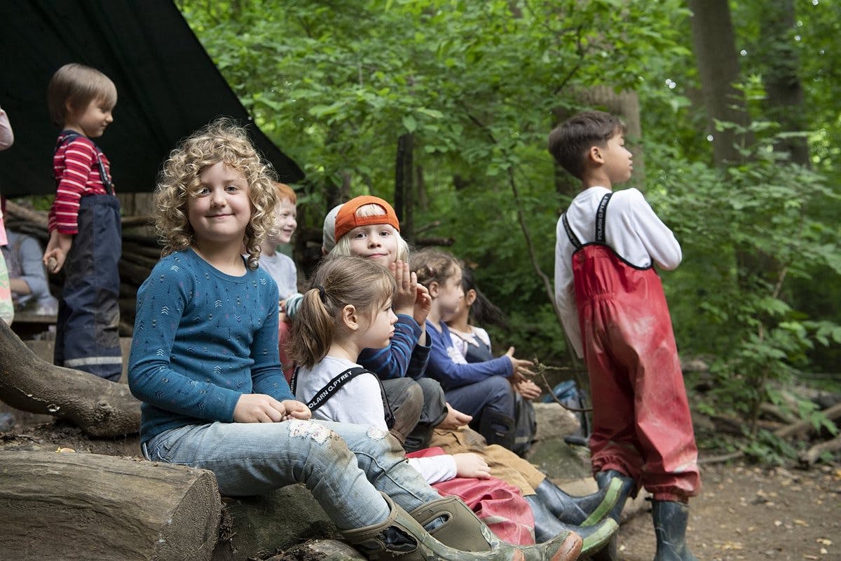Children sitting and standing outdoors in a wooded area