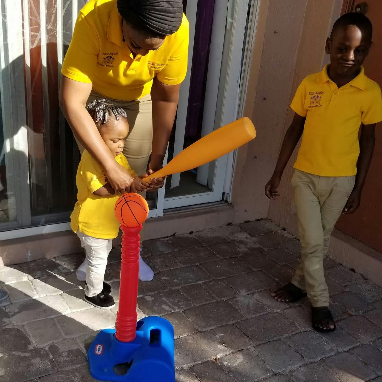 Person helping a child hit a ball on a tee with a bat