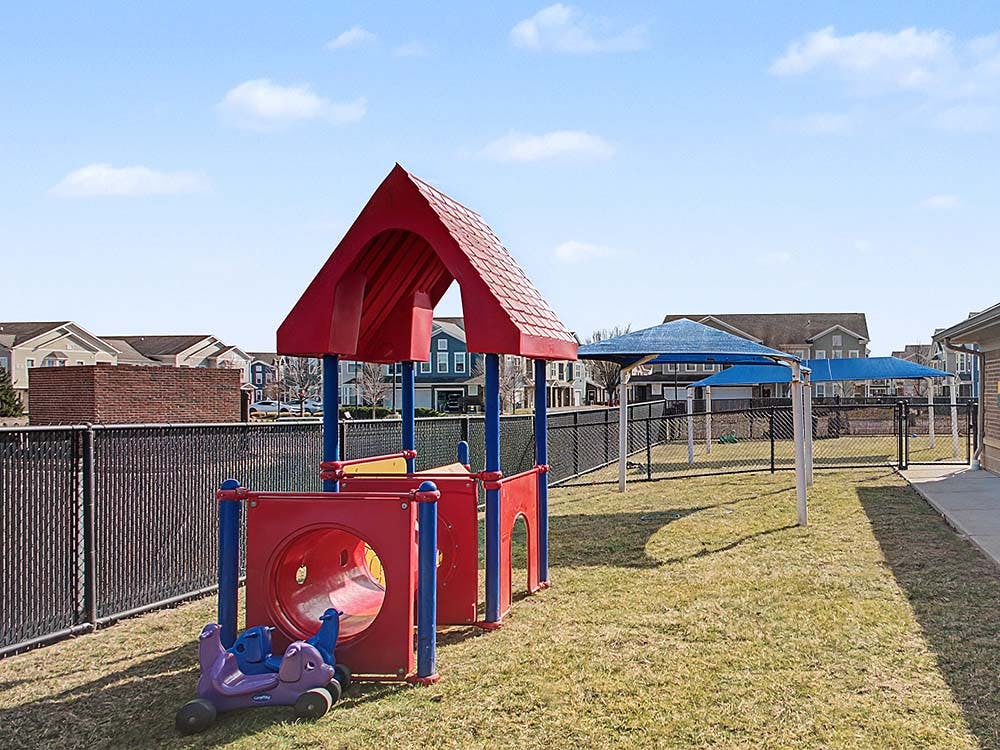 Red and blue playground equipment in a fenced-in grassy area
