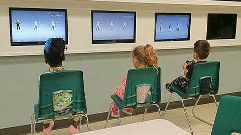 Three children sitting in chairs watching screens