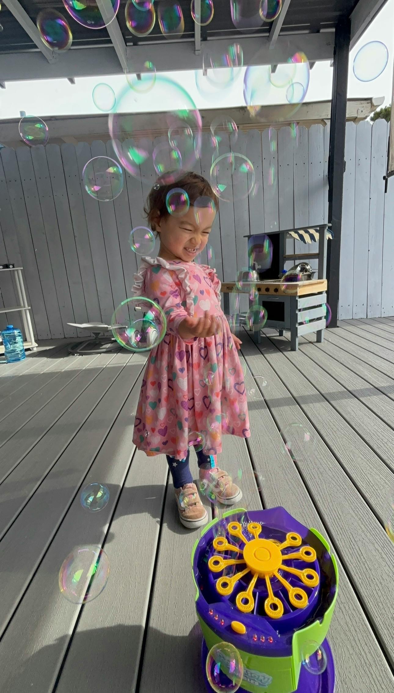 Child playing with a bubble machine on a wooden deck