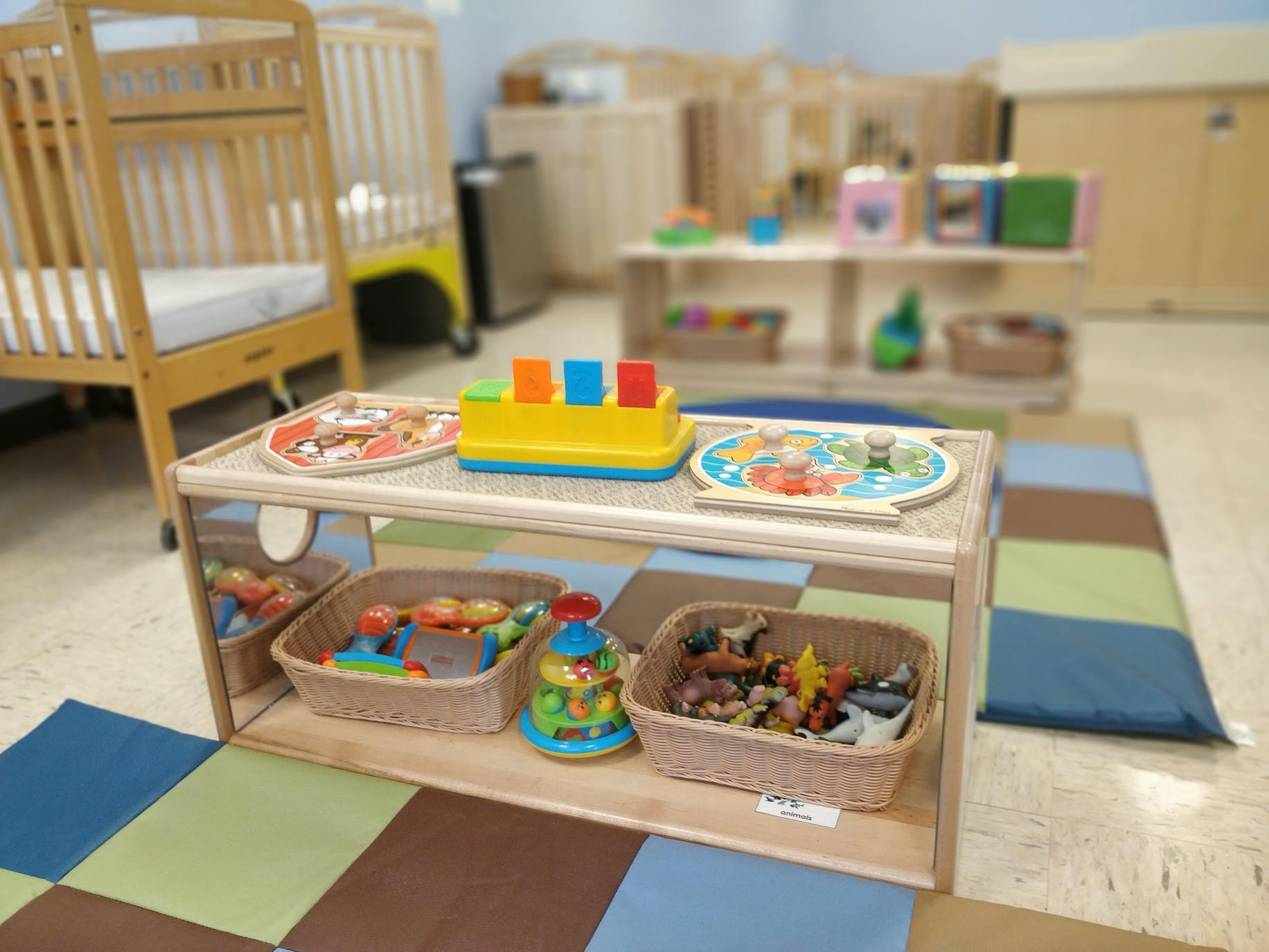 Playroom with wooden toy shelf, cribs, and colorful floor mats