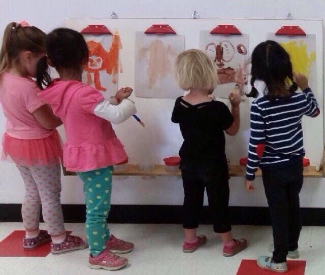 Four children painting at easels in a classroom