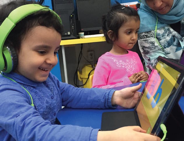 Child wearing headphones using a tablet with another child watching
