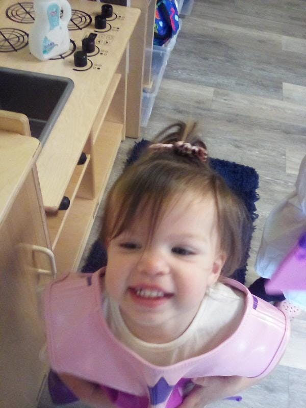 Child smiling in a pink bib, looking up at the camera