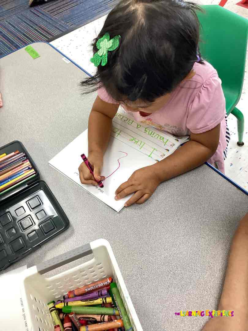Child drawing on paper with a red crayon at a table