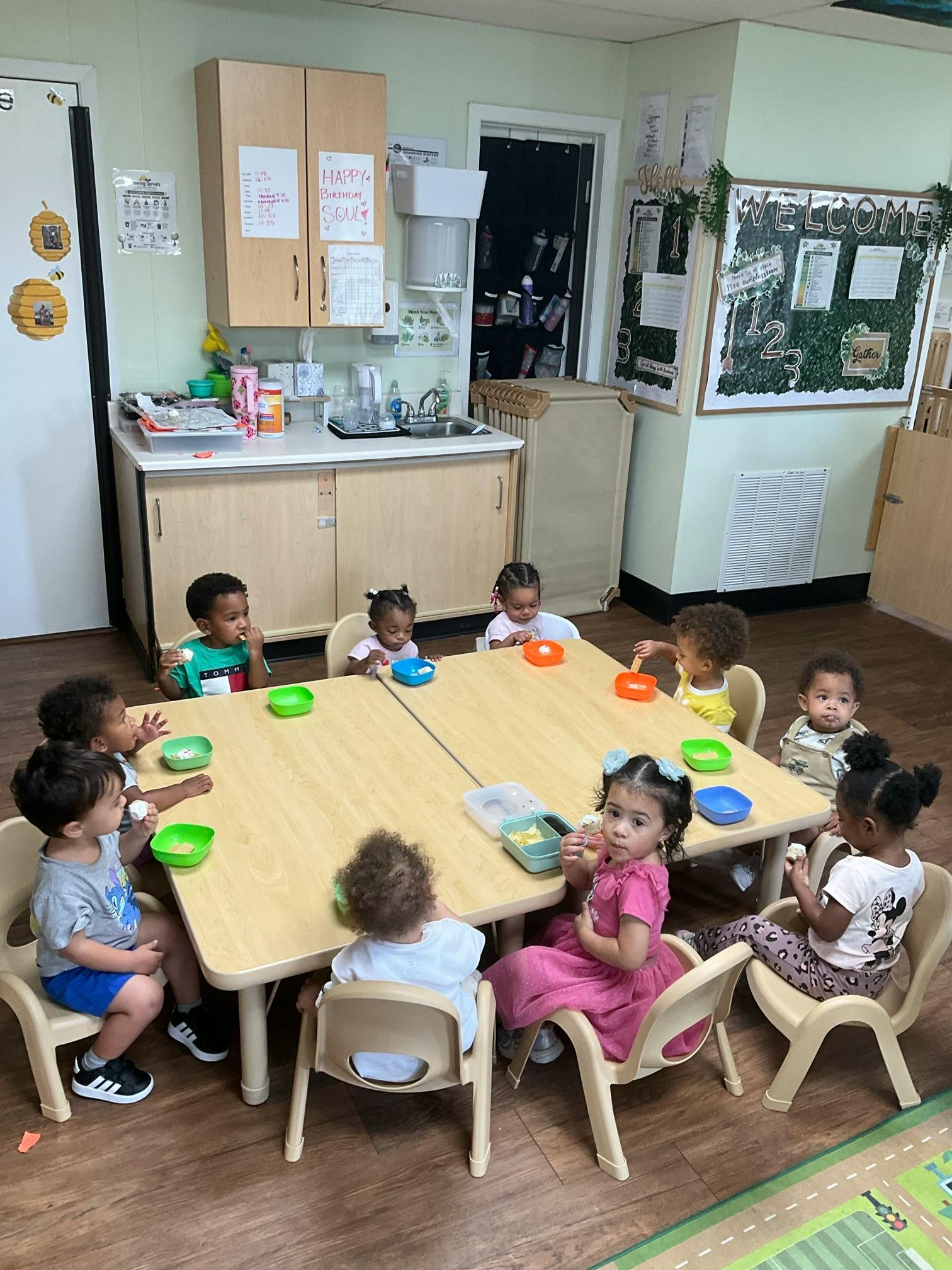 Group of children sitting at a table in a classroom eating snacks