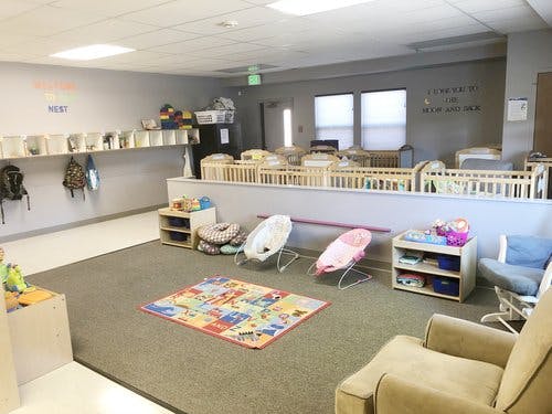 Daycare room with cribs, infant seats, and a colorful play mat