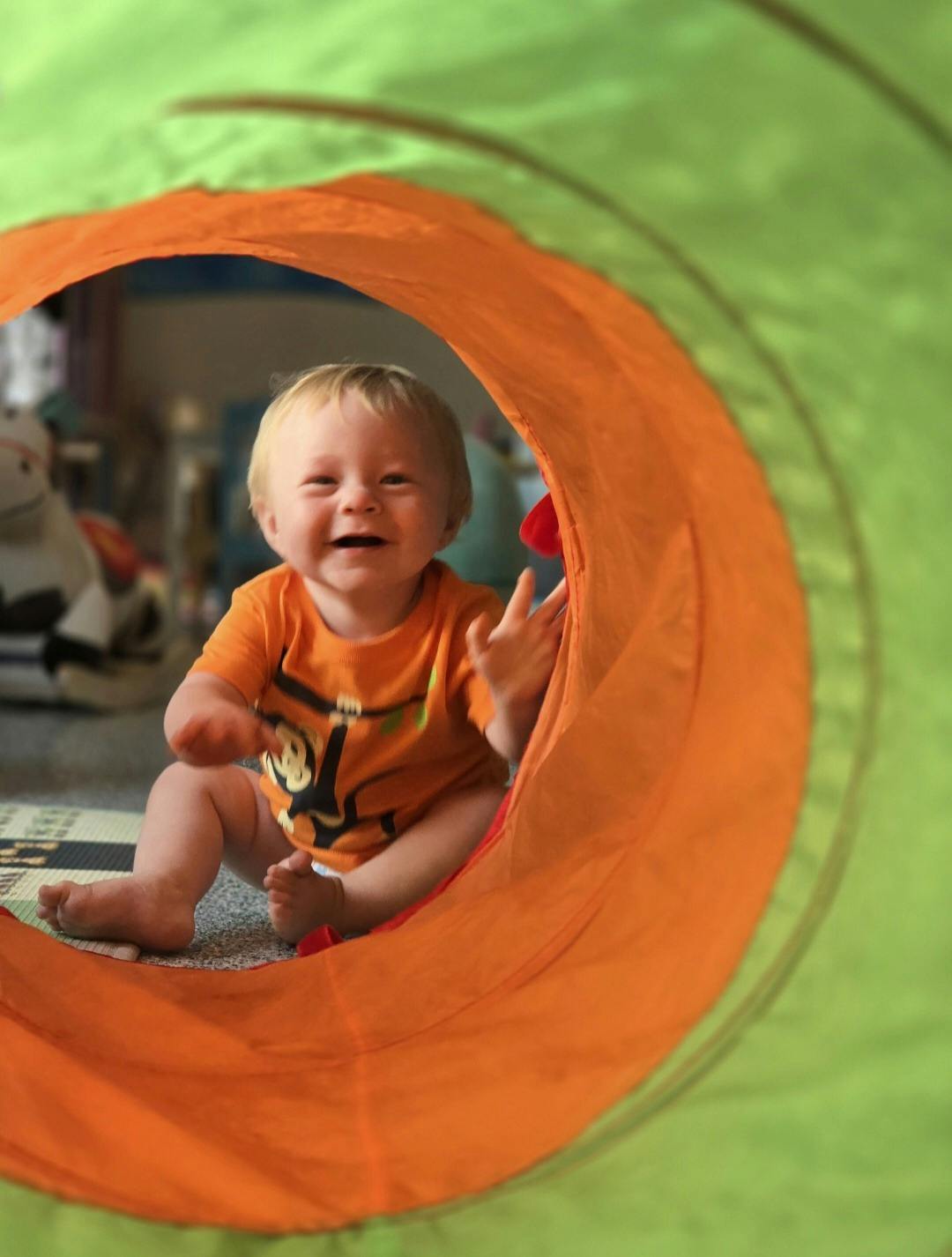 Child in an orange shirt emerging from a green and orange play tunnel