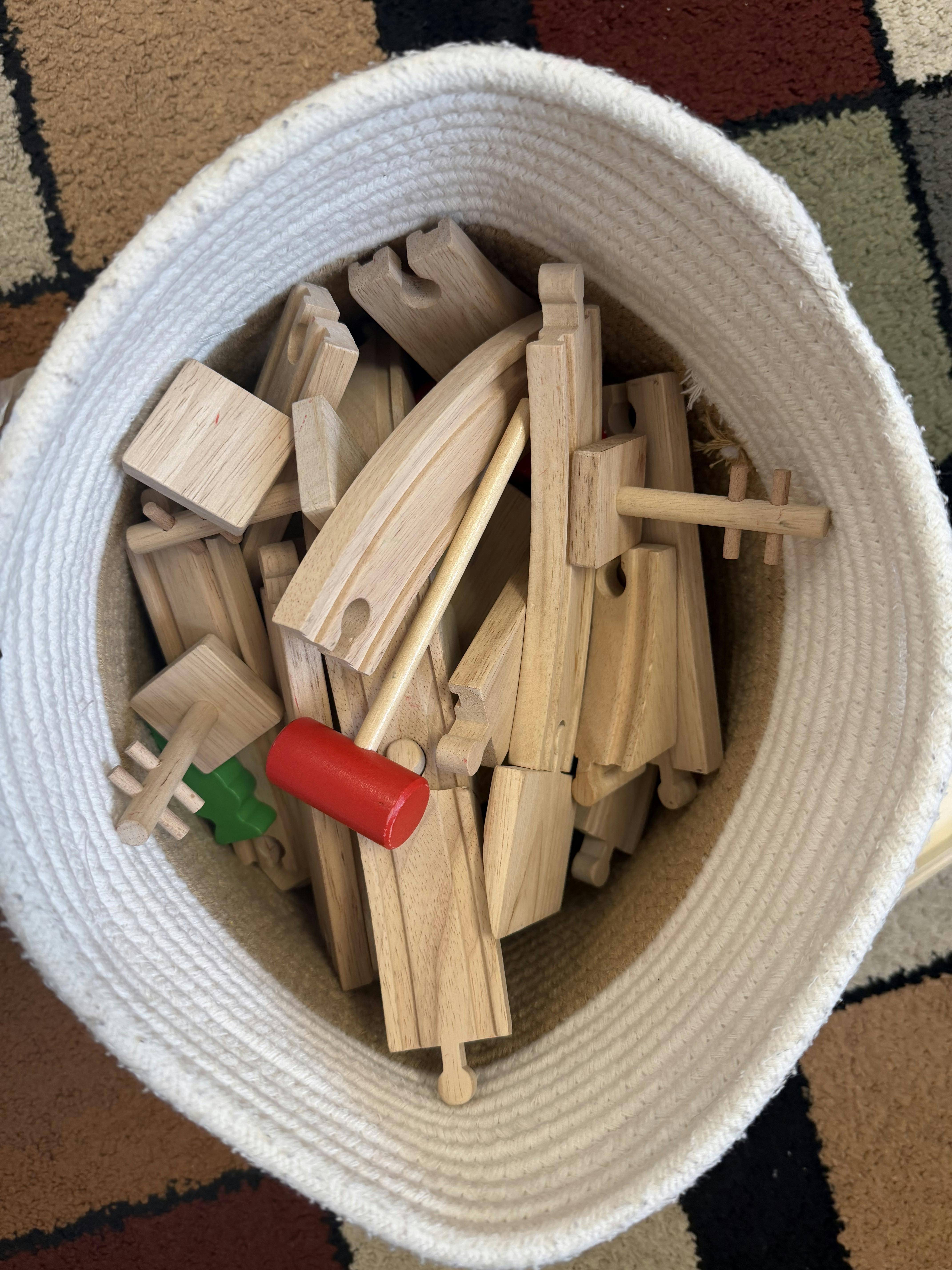 Wooden toy train tracks and pieces inside a fabric storage basket