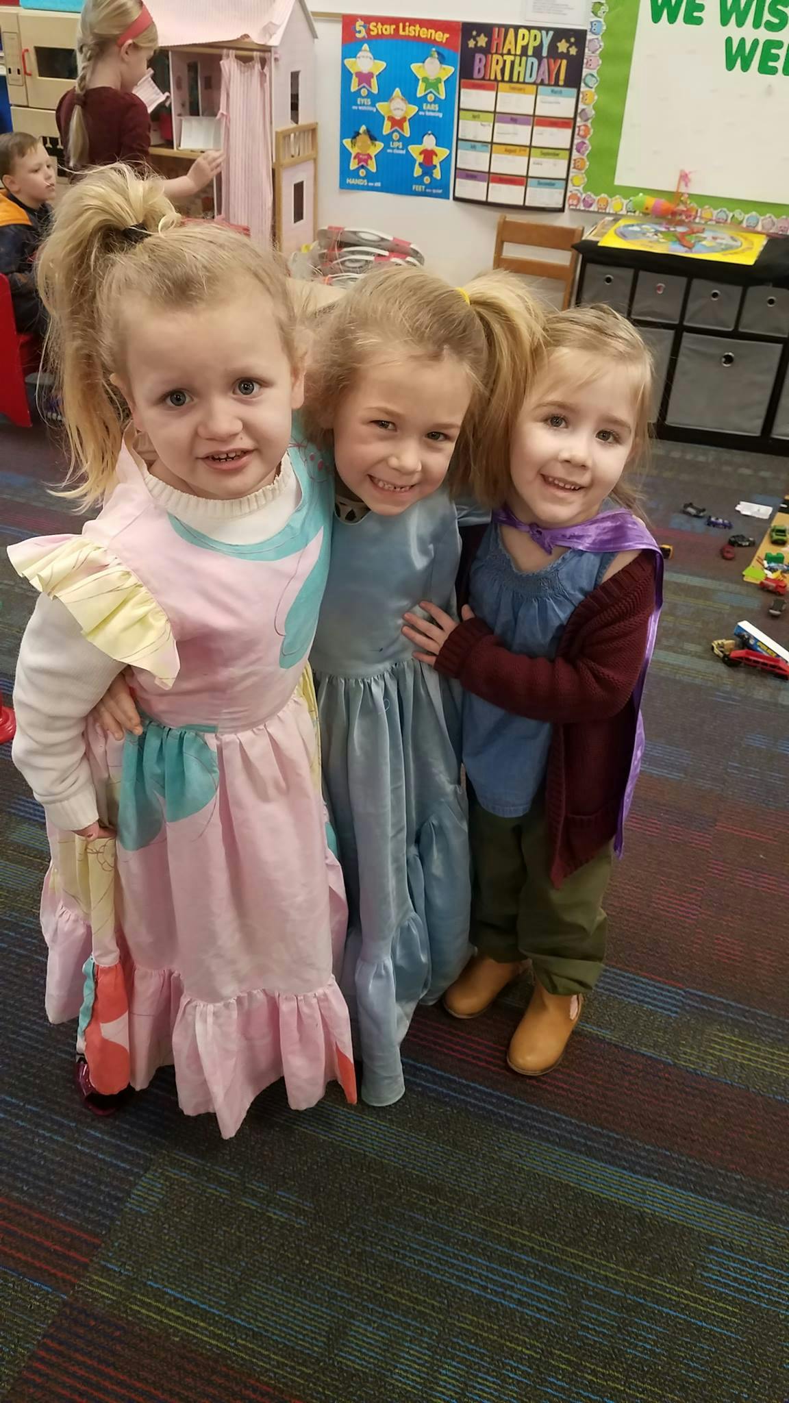 Three children in costumes standing together in a classroom