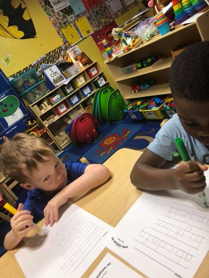 Two children writing at a table in a classroom