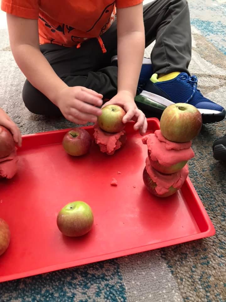 Child playing with apples and red playdough on a red tray