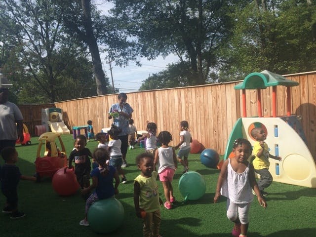 Adults supervising children playing with balls and playground equipment outdoors