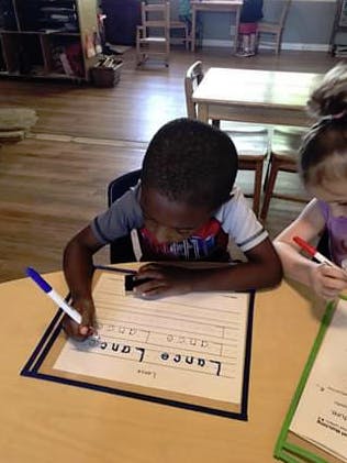 Child writing on a worksheet at a table in a classroom