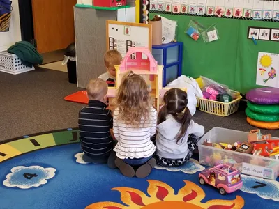 Children playing with a dollhouse in a classroom