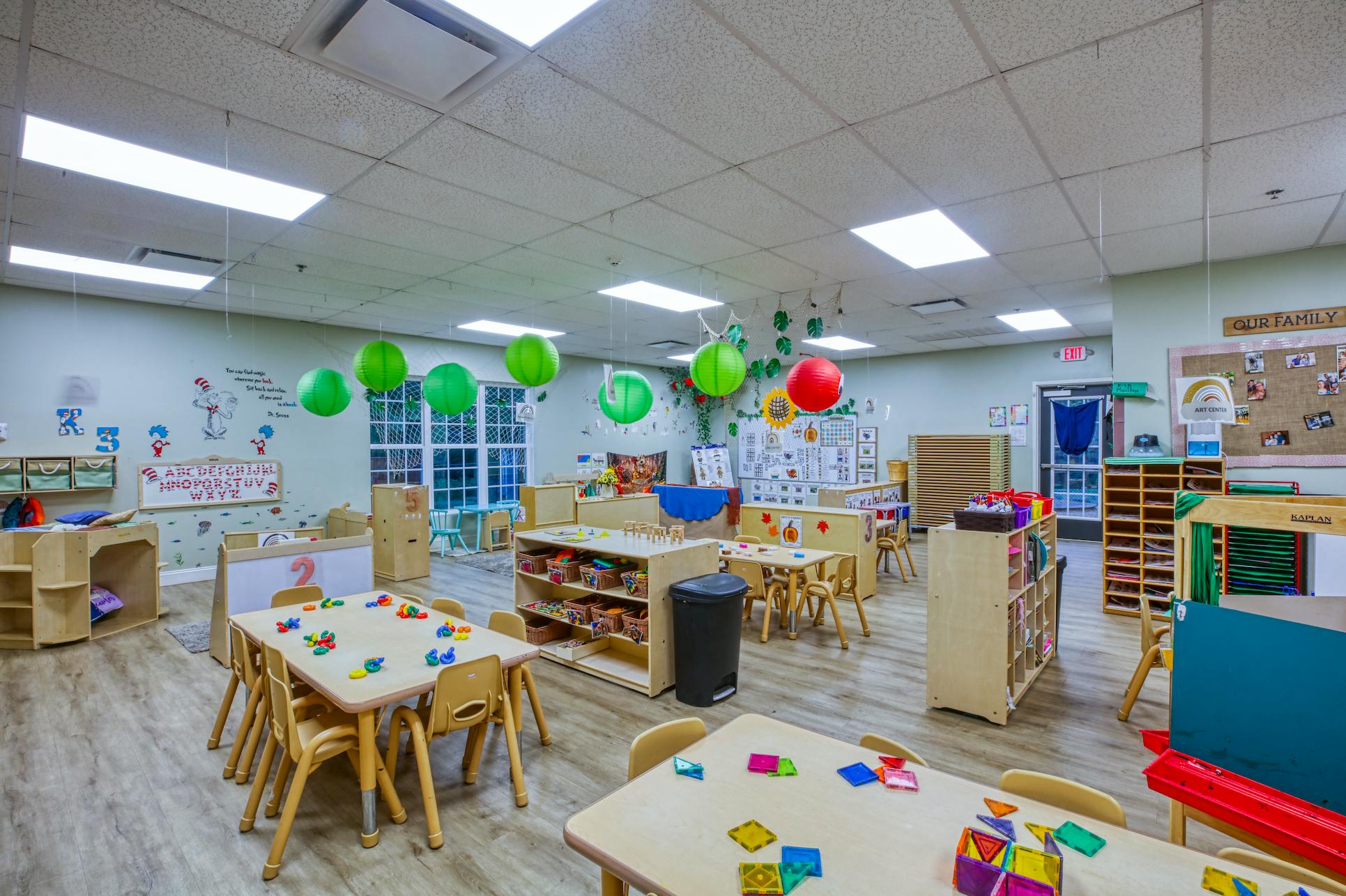 An empty classroom with several small tables and chairs for children