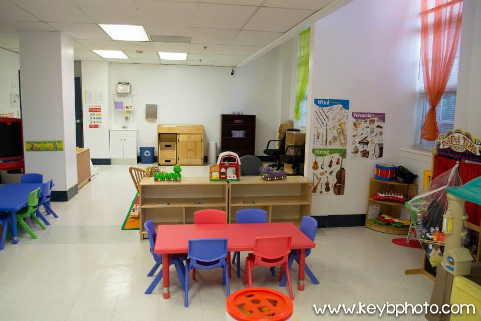 Classroom with small tables and chairs, shelves with toys, and posters on the wall