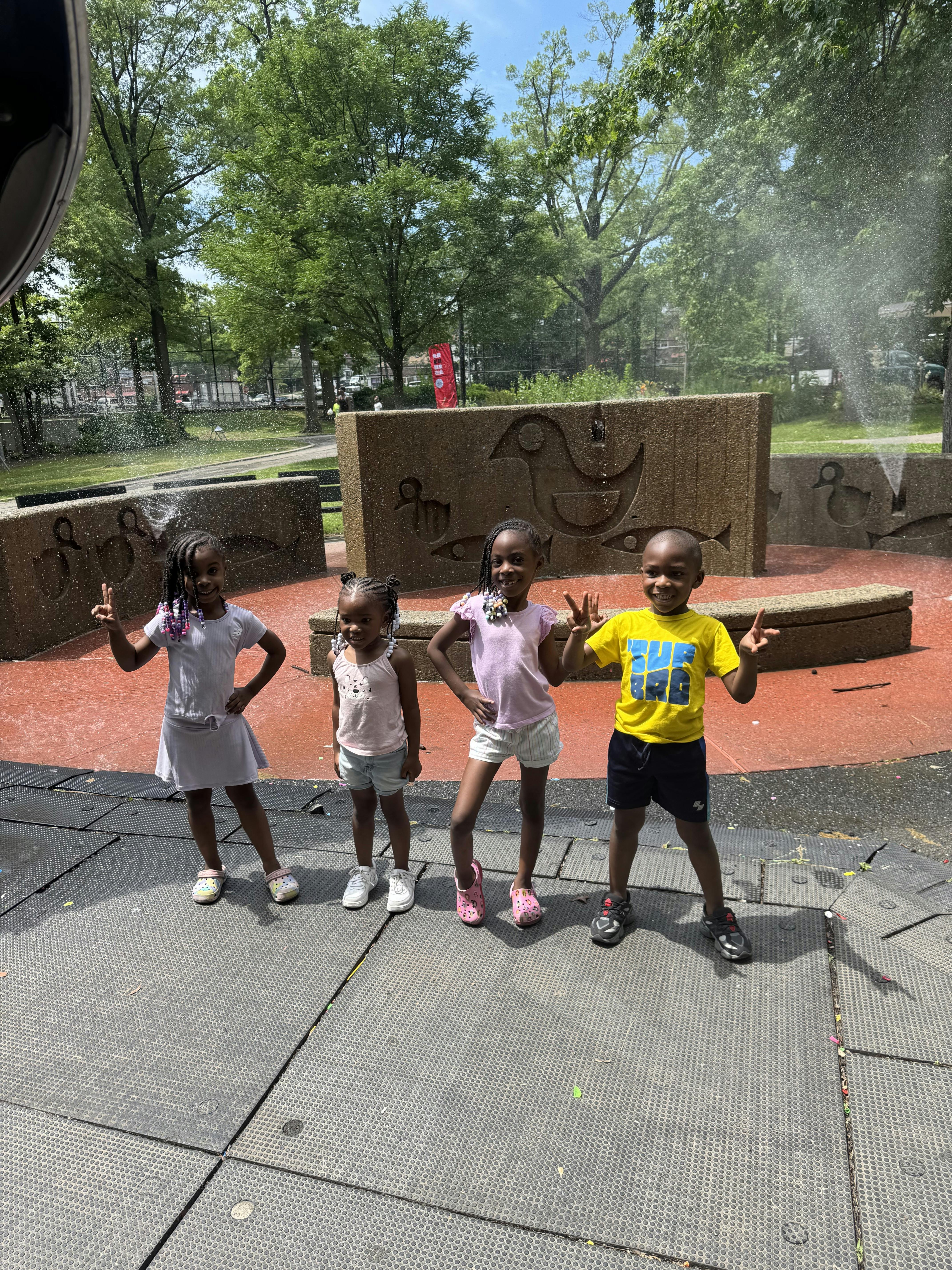 Four children standing in front of a fountain, two flashing peace signs