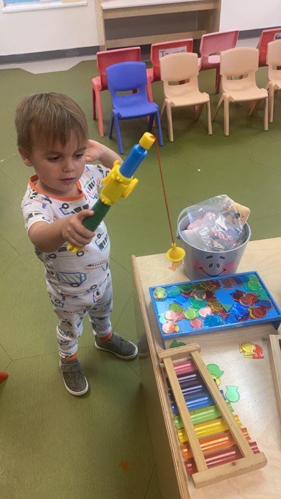 Child holding a toy fishing rod in a classroom