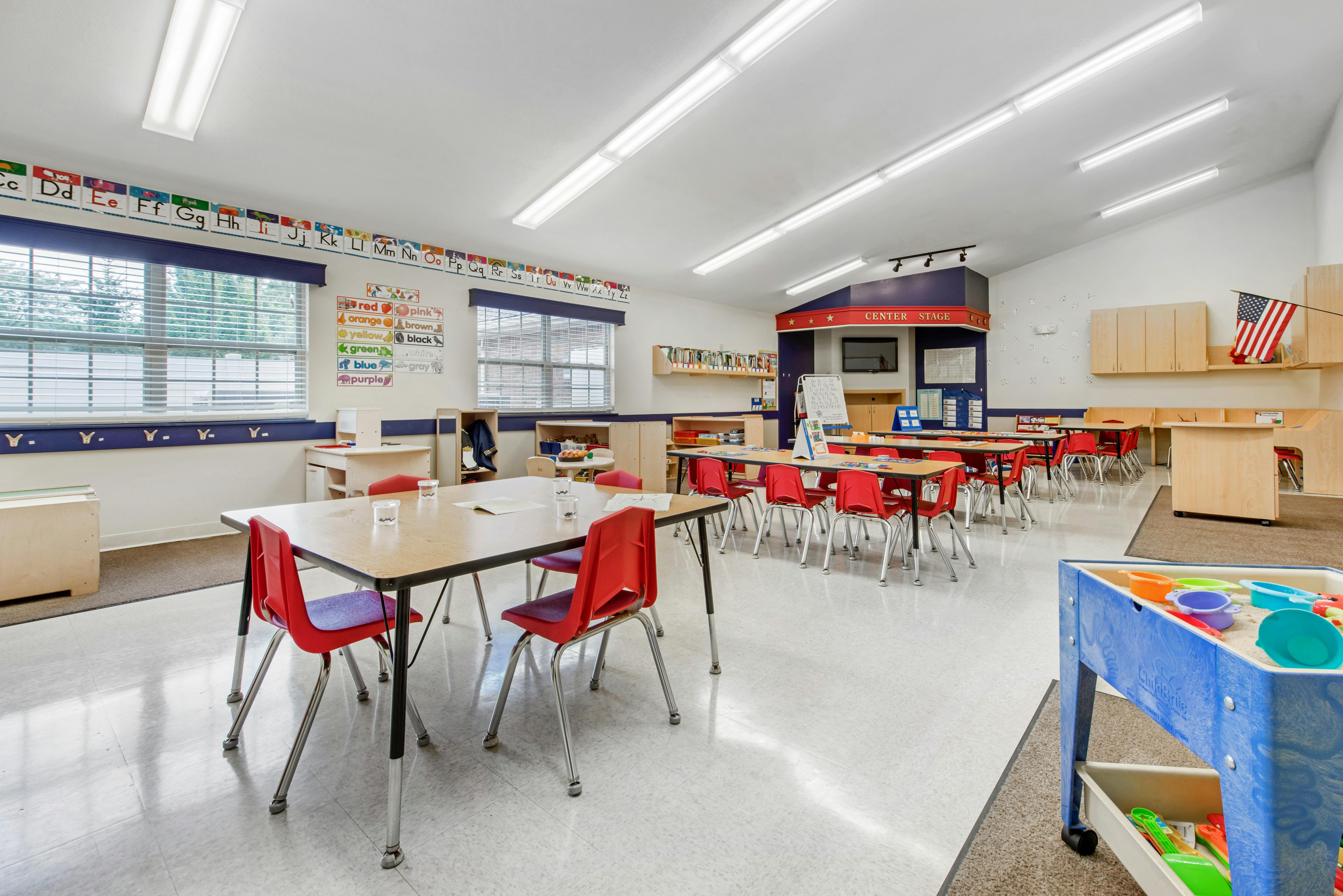 Empty classroom with small red chairs at wooden tables and alphabet on the wall