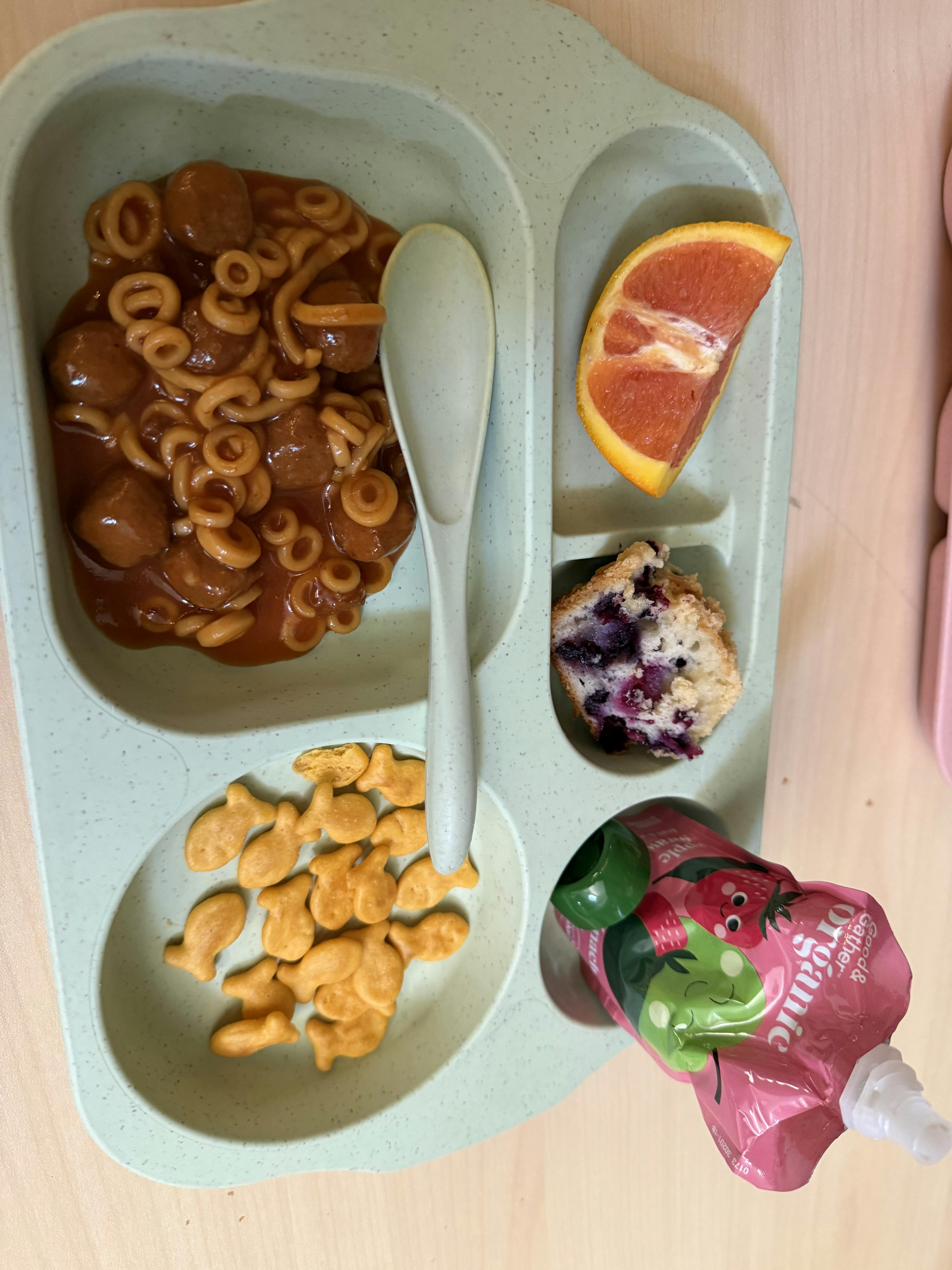 A divided serving plate with spaghetti and meatballs, goldfish crackers, a muffin, and grapefruit