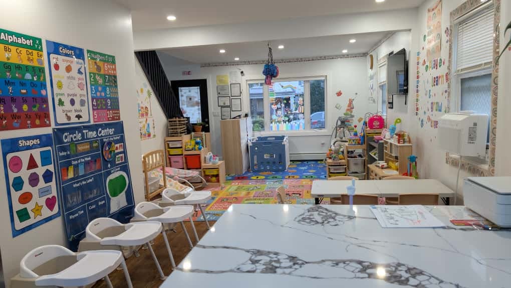 Playroom with colorful alphabet and shapes posters on wall, high chairs, and toys