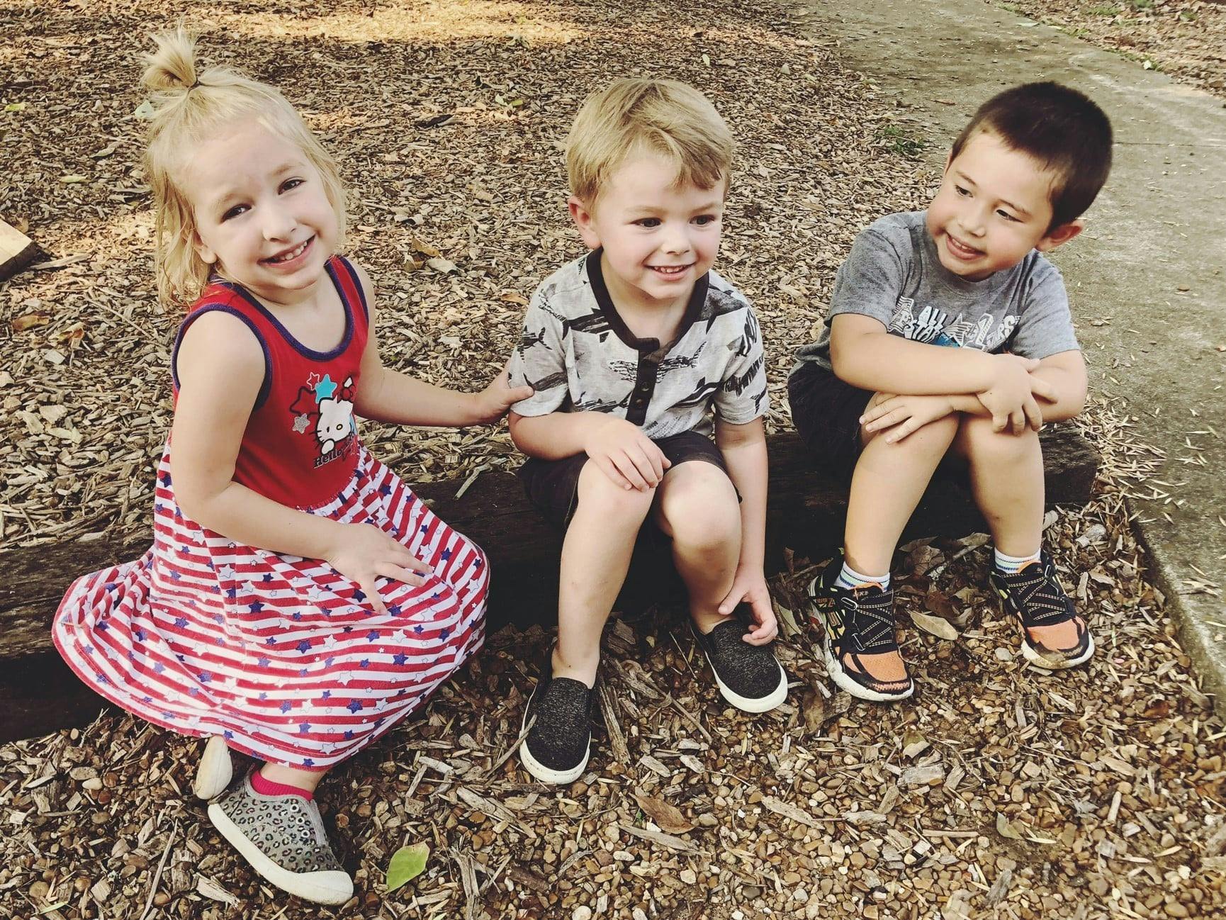 Three children sitting on wood chips