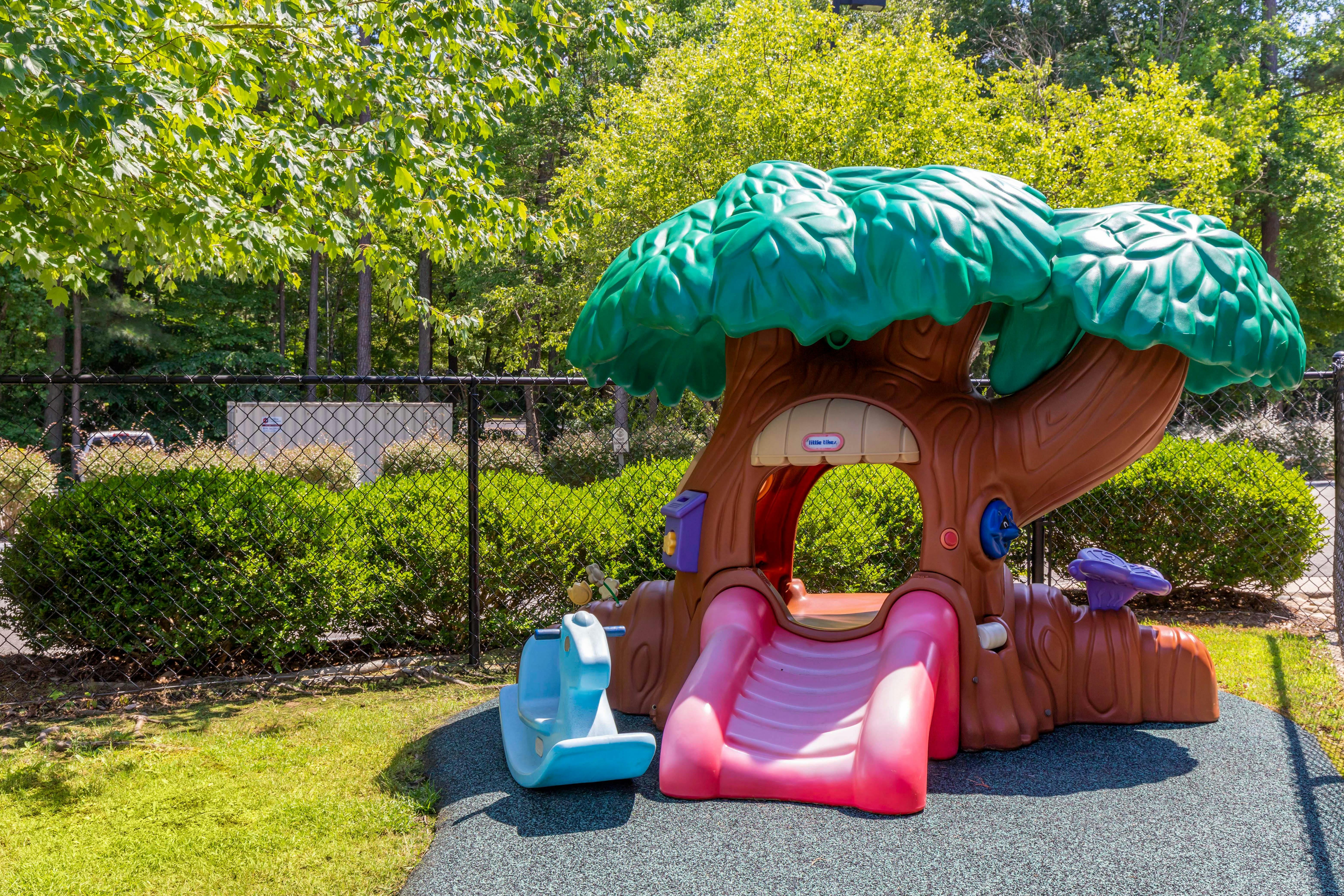 Plastic treehouse-shaped play structure with a pink slide and blue rocking horse