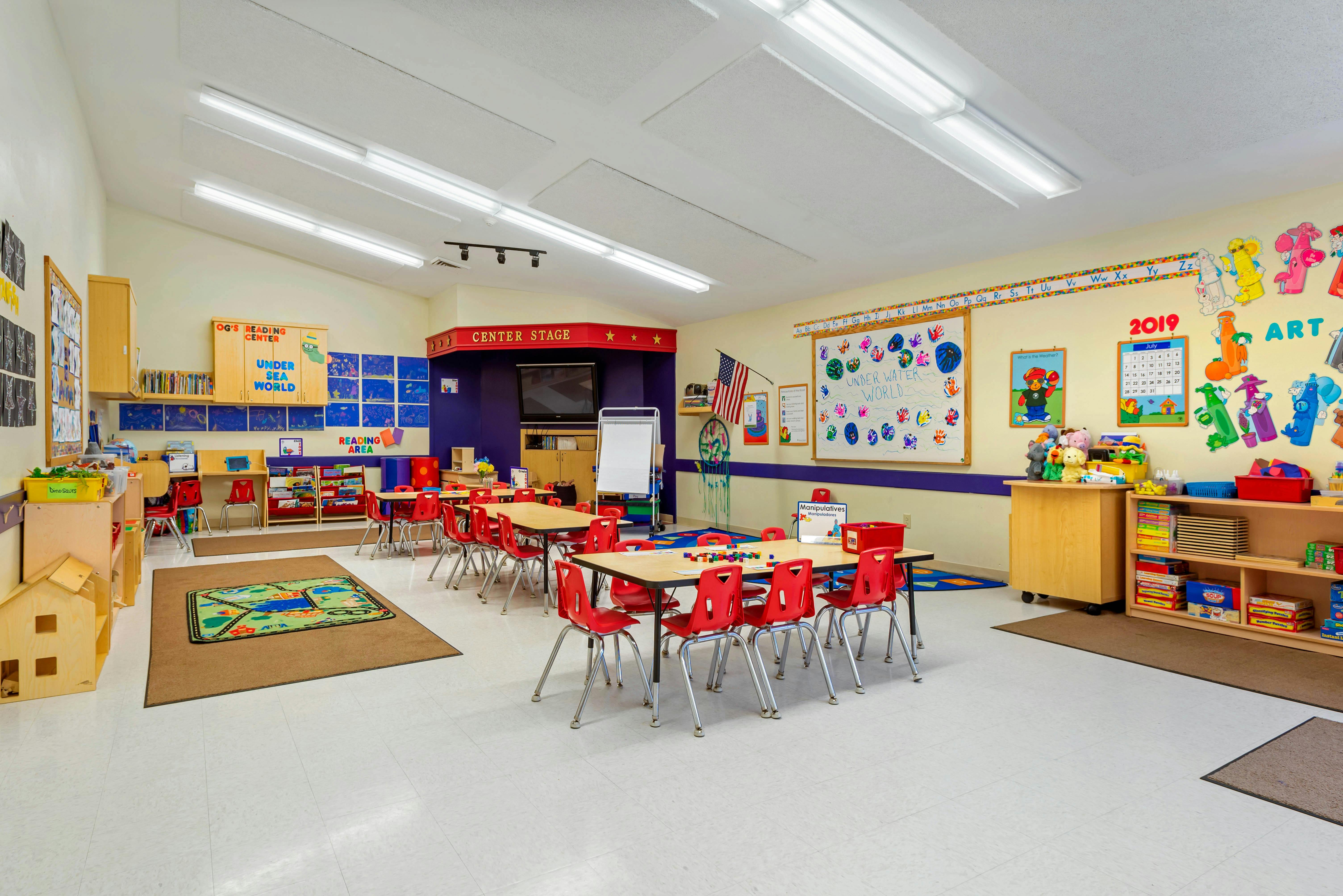 Classroom with child-sized tables and chairs, reading corner, and art display