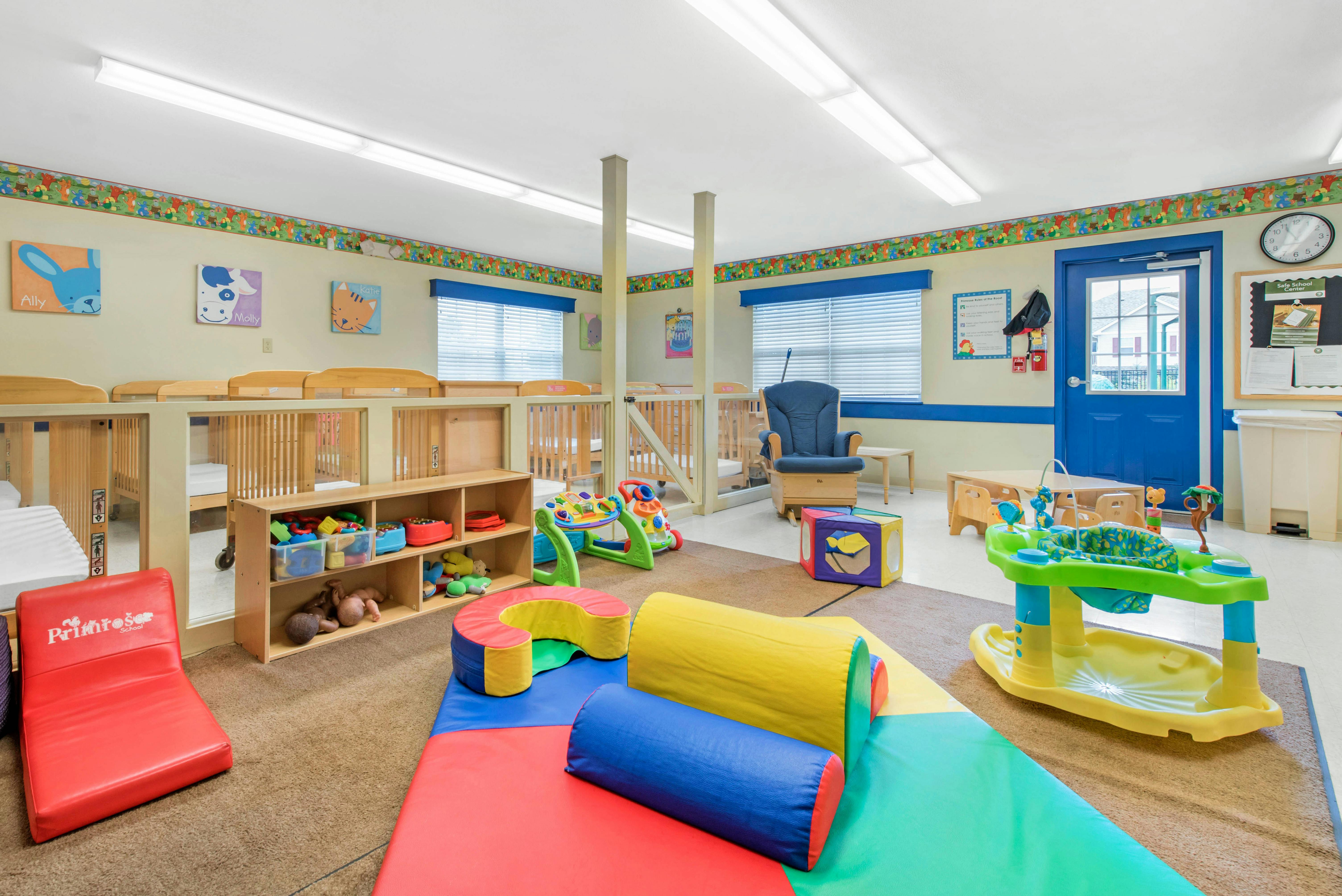 A childcare center classroom with cribs, play mats, and toys