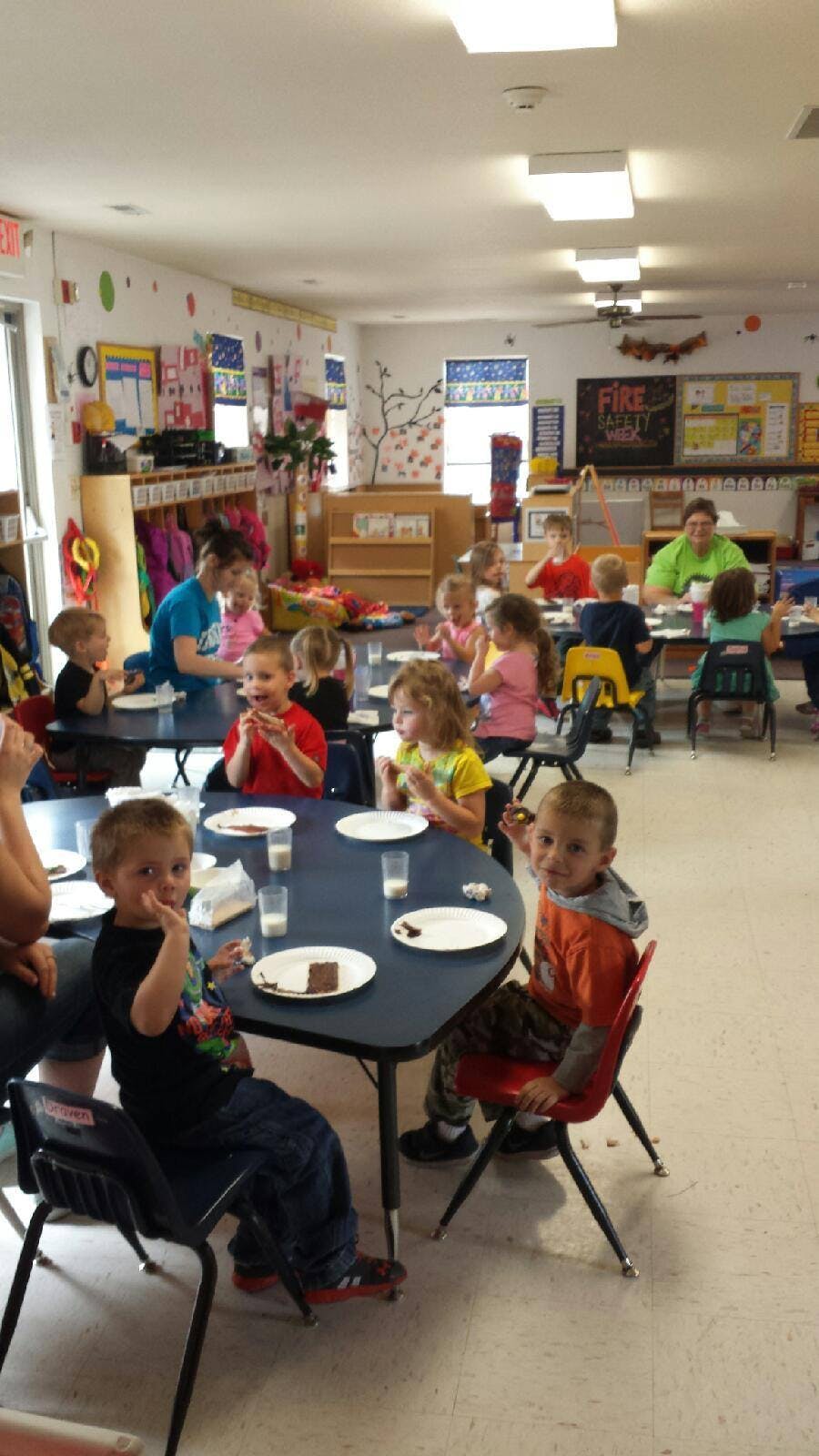 Children and adults eating at tables in a classroom