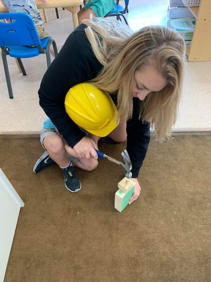Person in a yellow hard hat hammering a block of wood