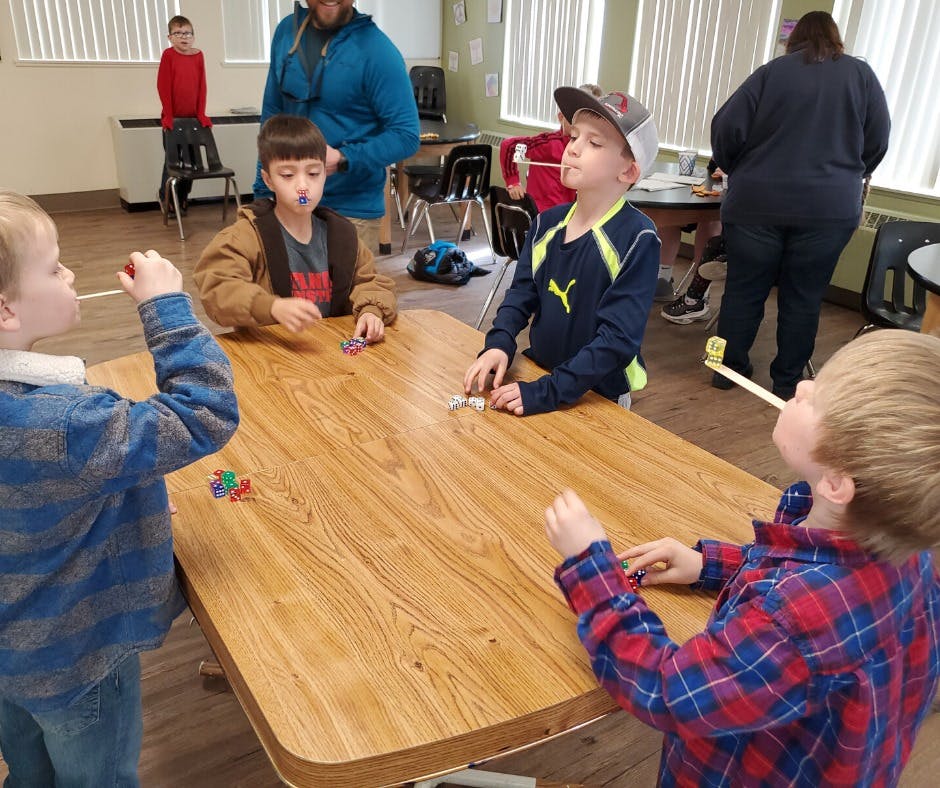 Children playing a game with straws and small objects on a table