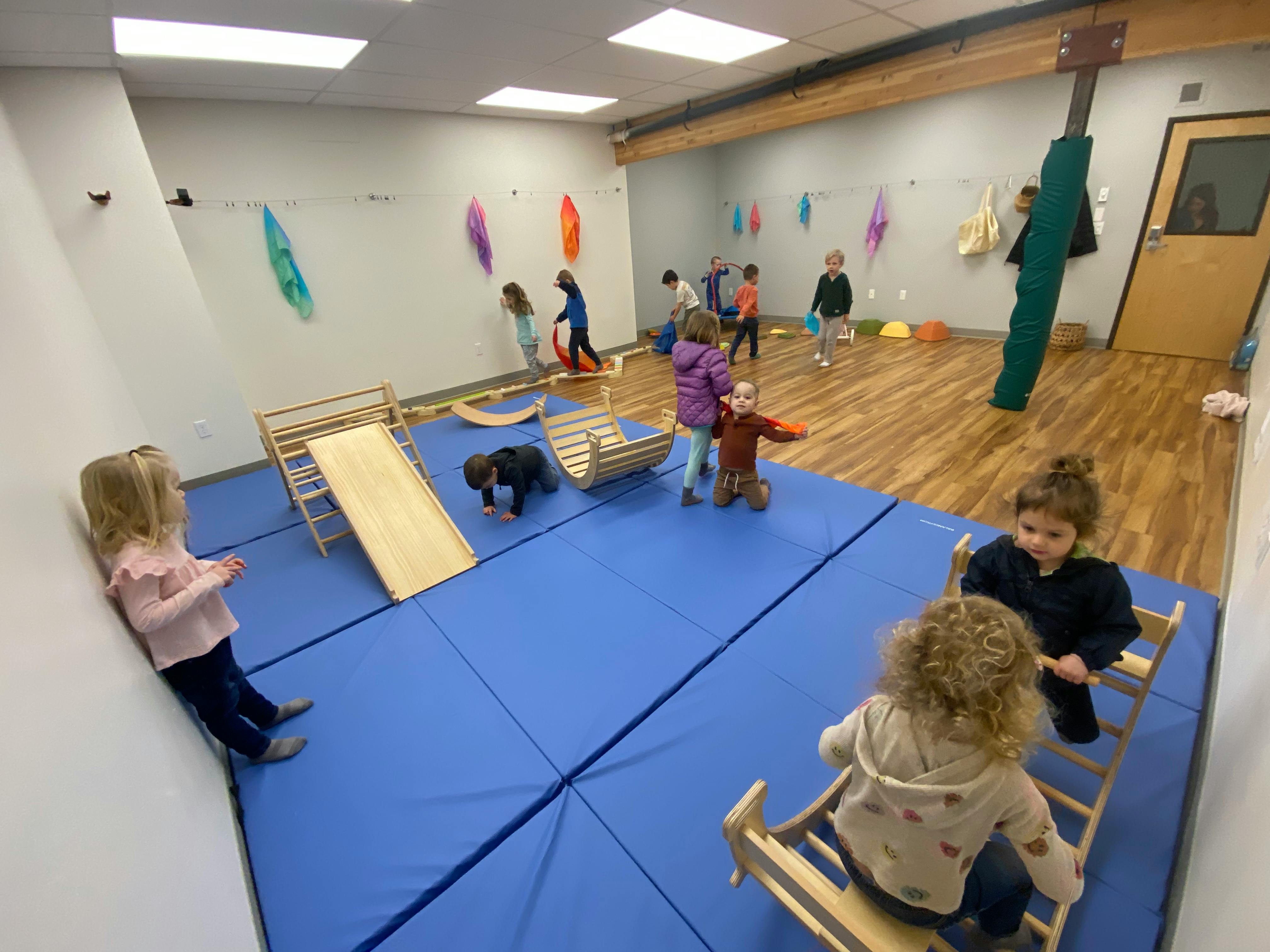 Children playing in a room with blue mats and wooden play equipment