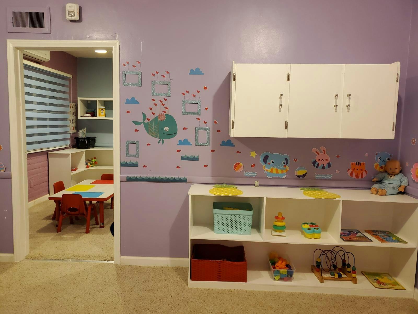 Playroom with purple walls, shelves of toys, and a small table with chairs