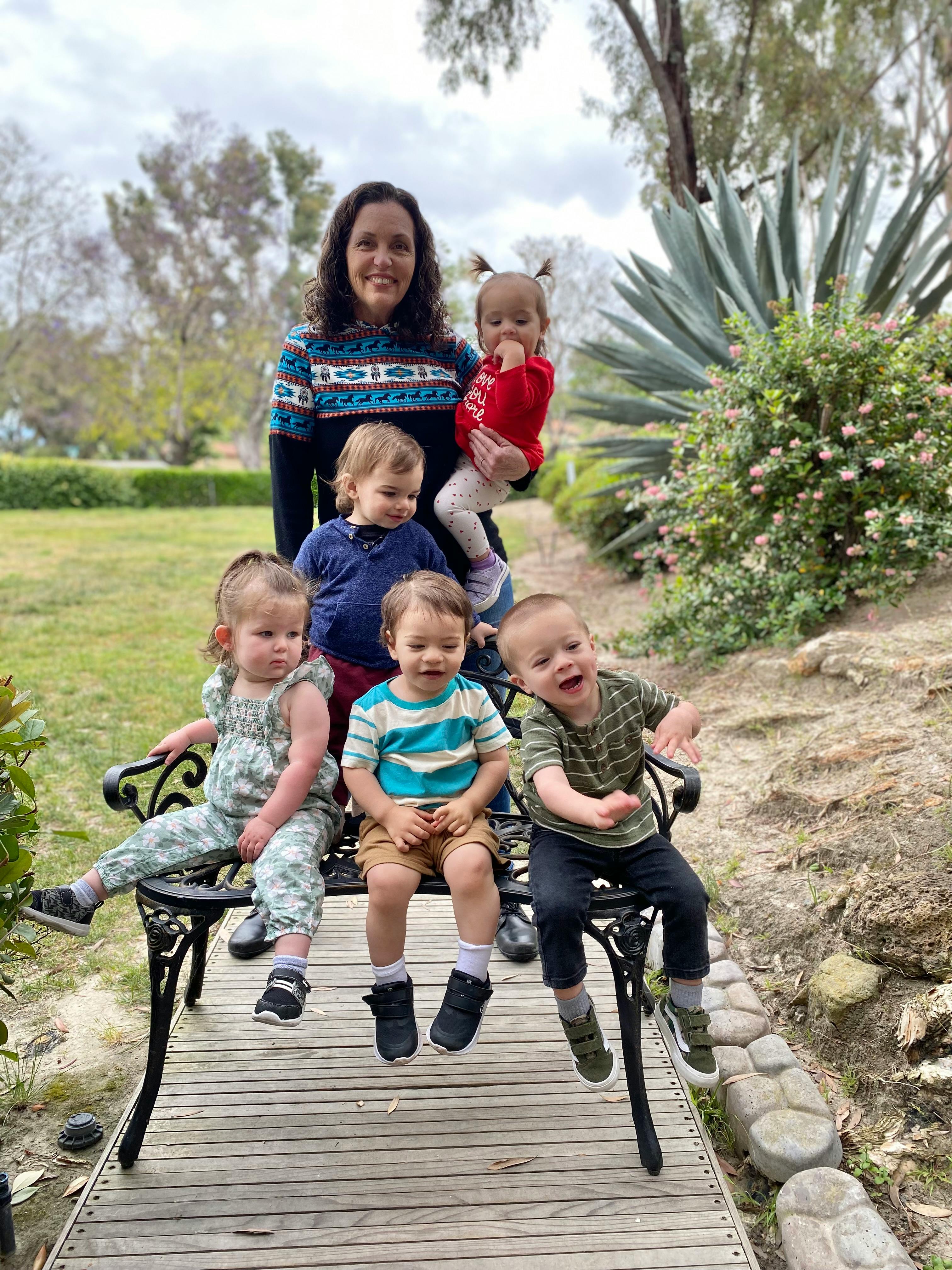 Person holding a child, with four other children sitting on a bench