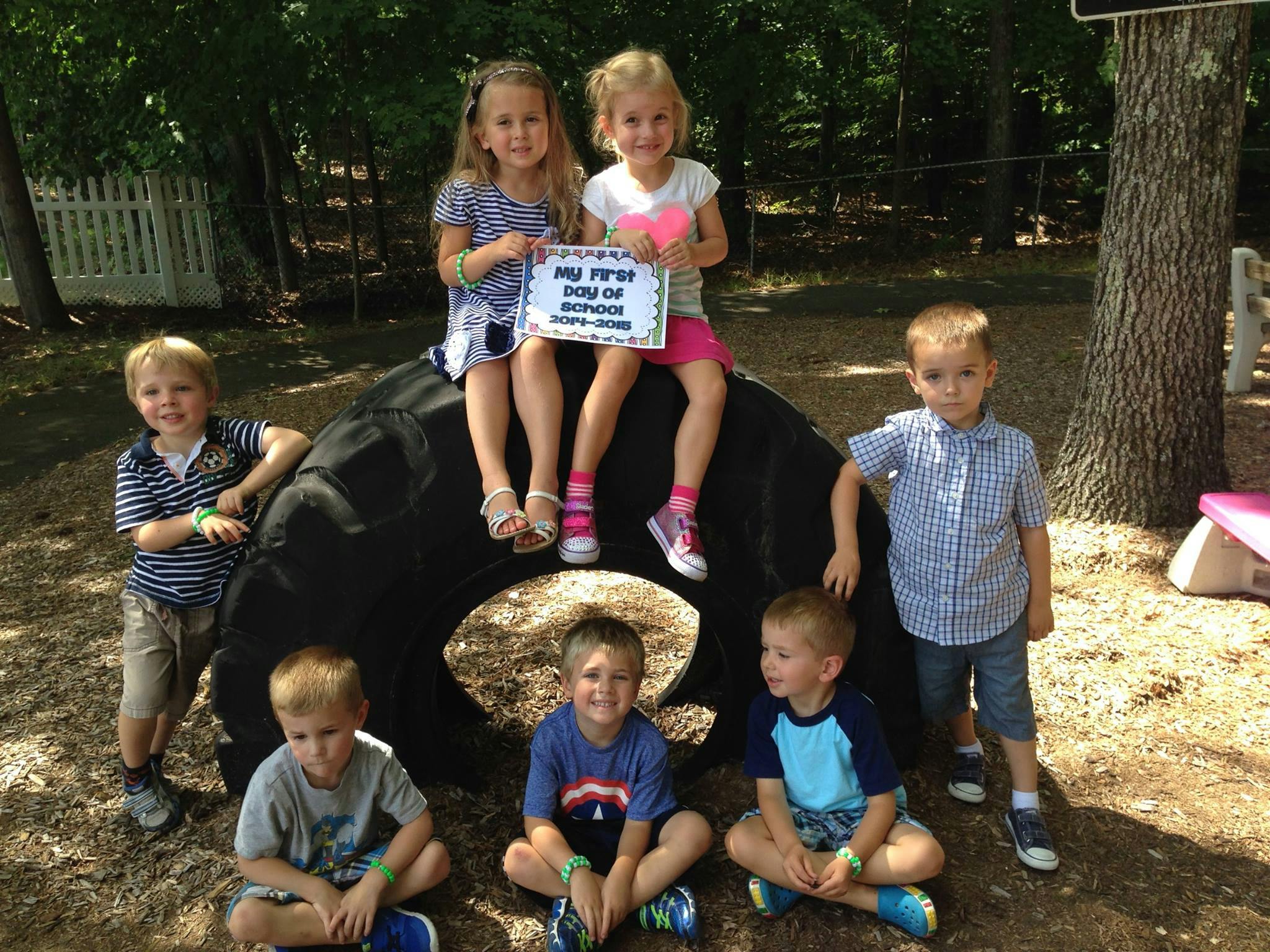 Six children posing around a large tire, two holding a sign