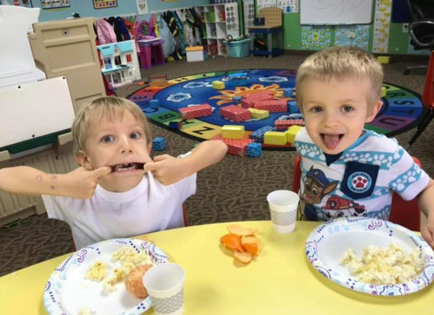 Two children at a table, one making a face and the other smiling