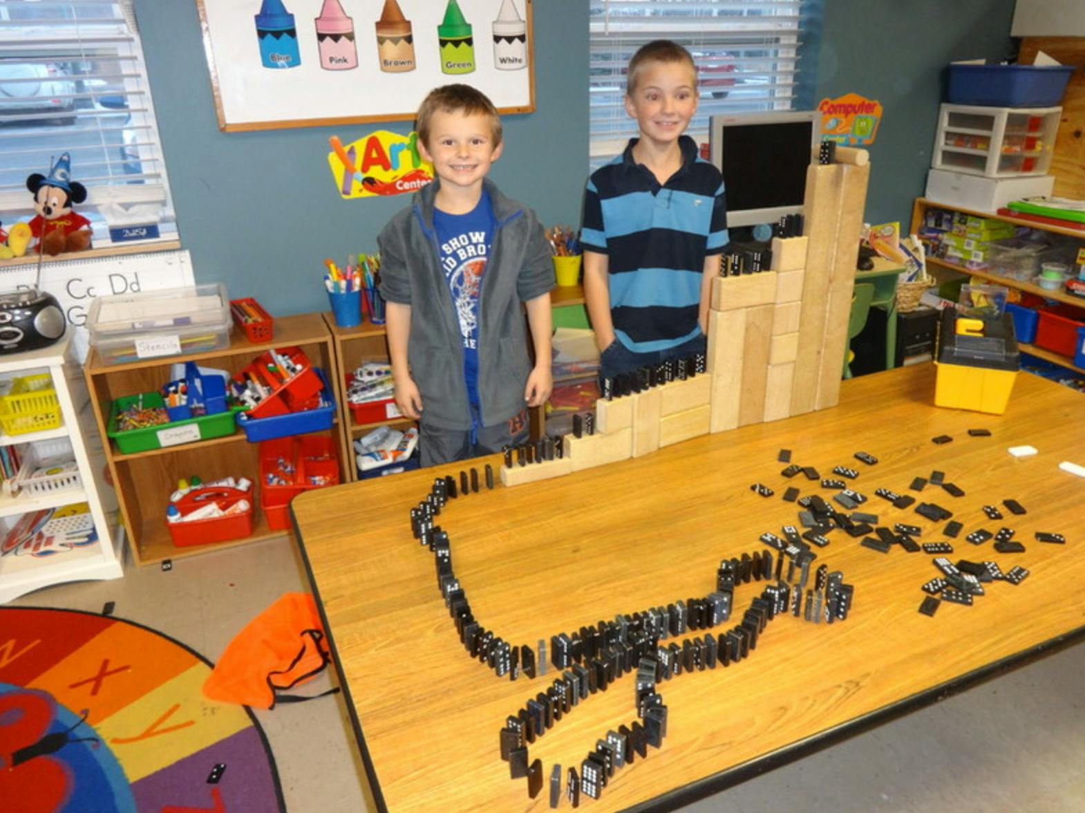 Two children standing behind a table with dominoes and wooden blocks