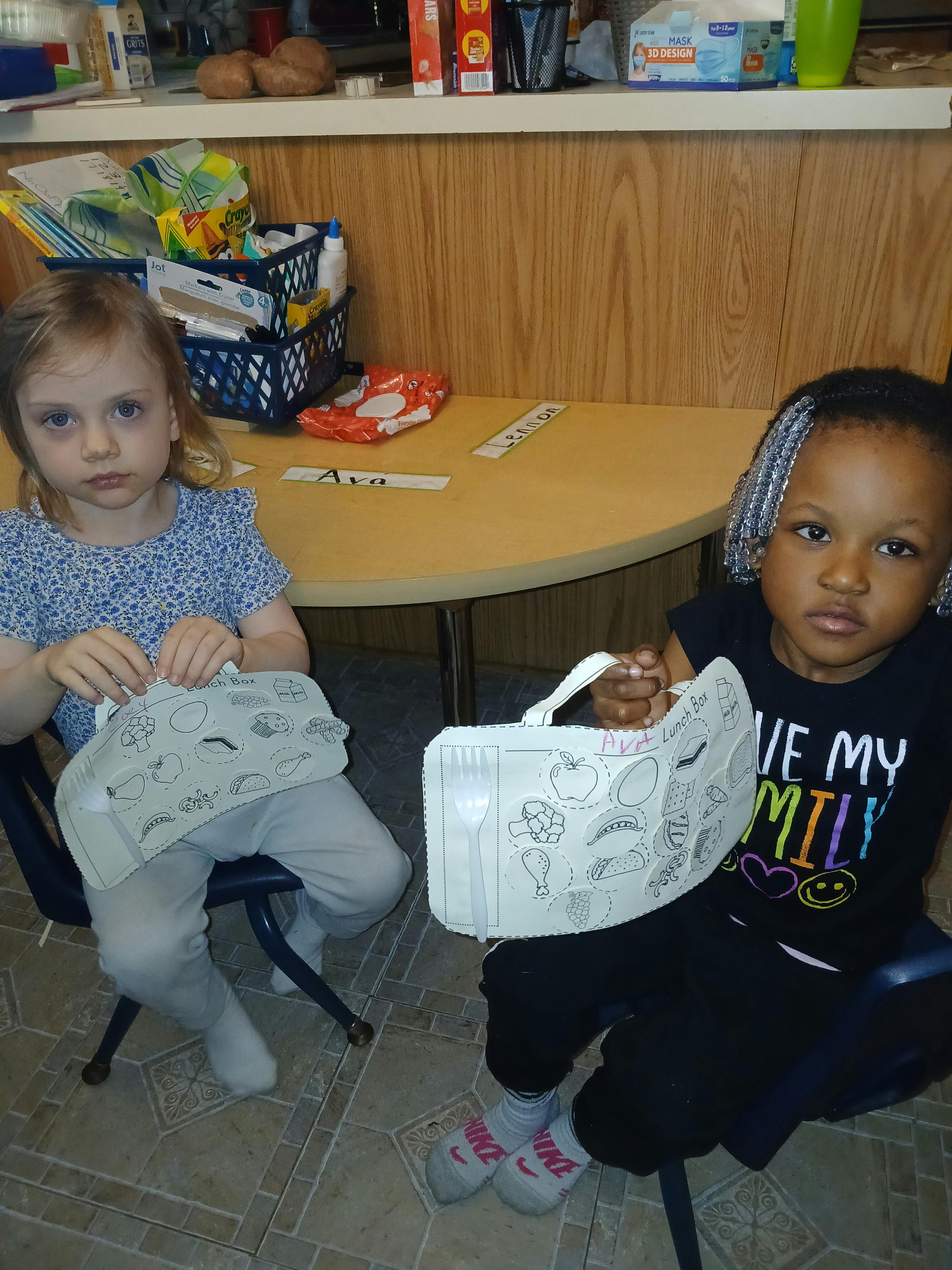 Two children sitting at a table holding craft projects